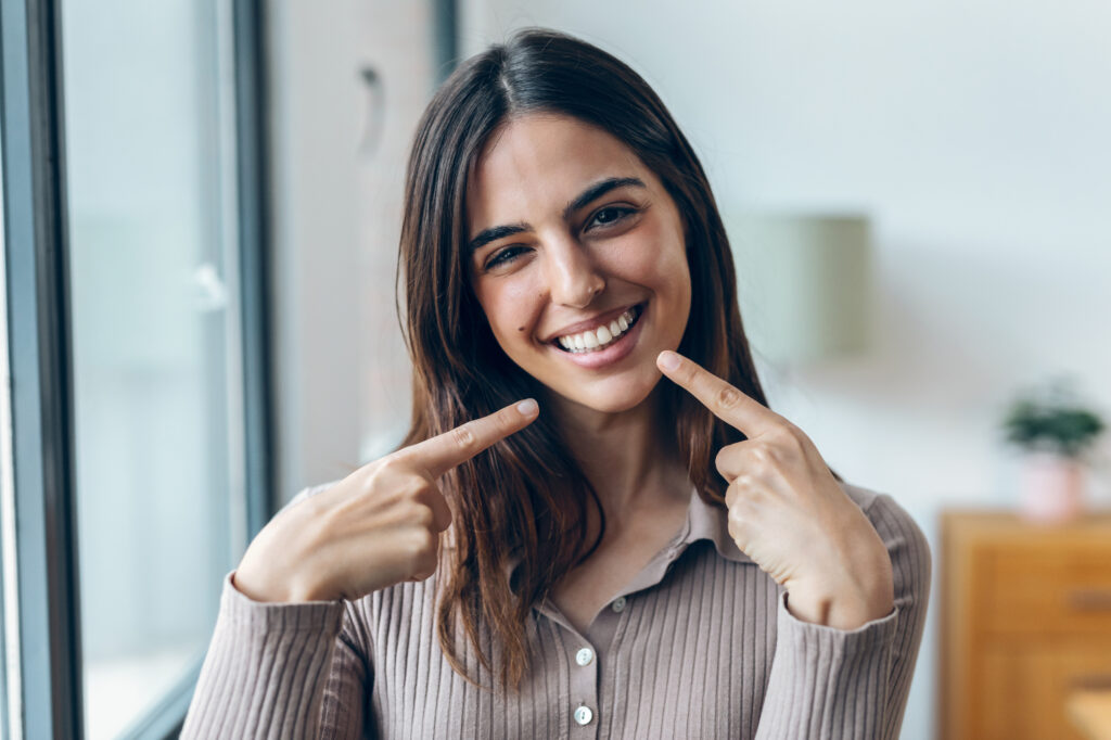 Young woman pointing to her smile, use your FSA for braces or Invisalign with Fellow Orthodontist in Union Square, Manhattan